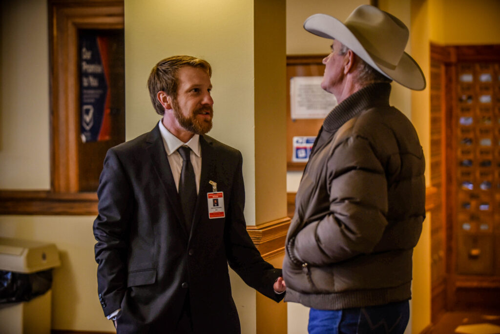 Montana Free Press education reporter Alex Sakariassen catches up with Choteau outfitter and rancher Dusty Crary inside the Montana Capitol during the 2023 legislative session. Photo by Eliza Anderson Wiley for Montana Free Press