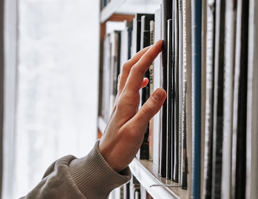 Hand reaching for books on shelf